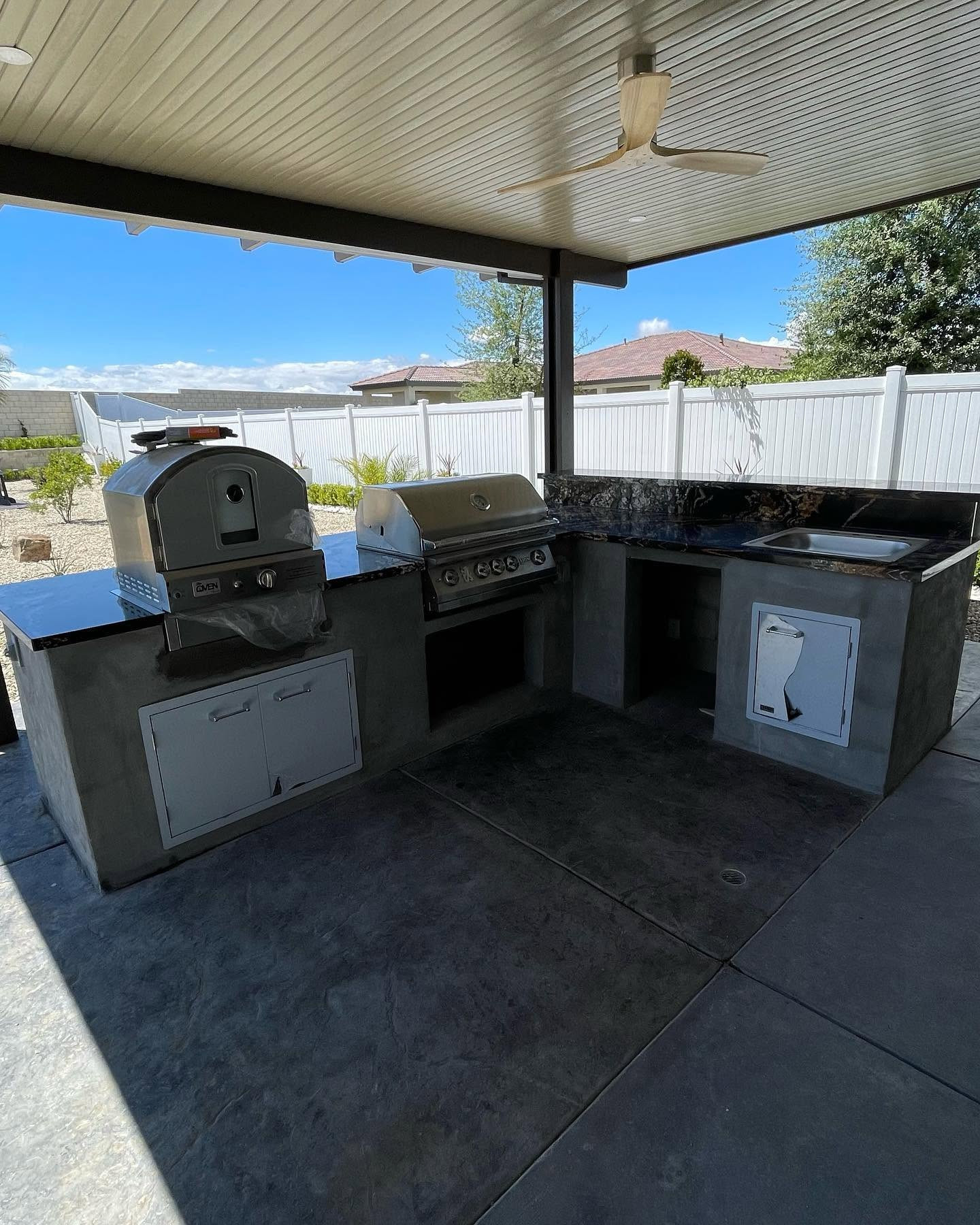 Outdoor kitchen with grill, pizza oven and black granite counters